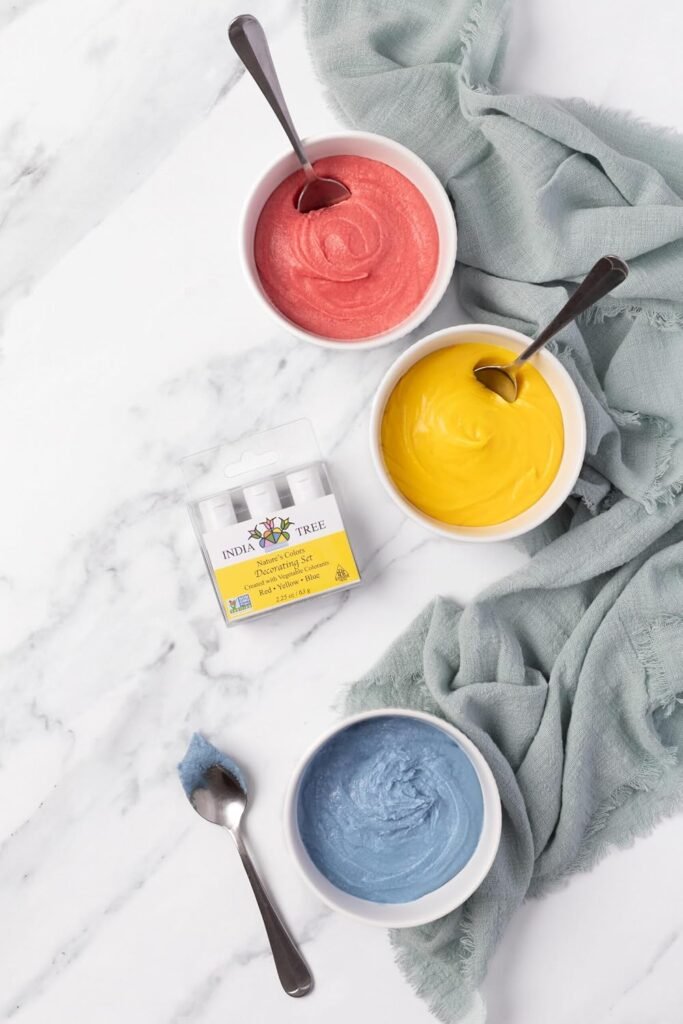 Four small glass bowls filled with colorful liquid food coloring dyes arranged on a grey marble surface