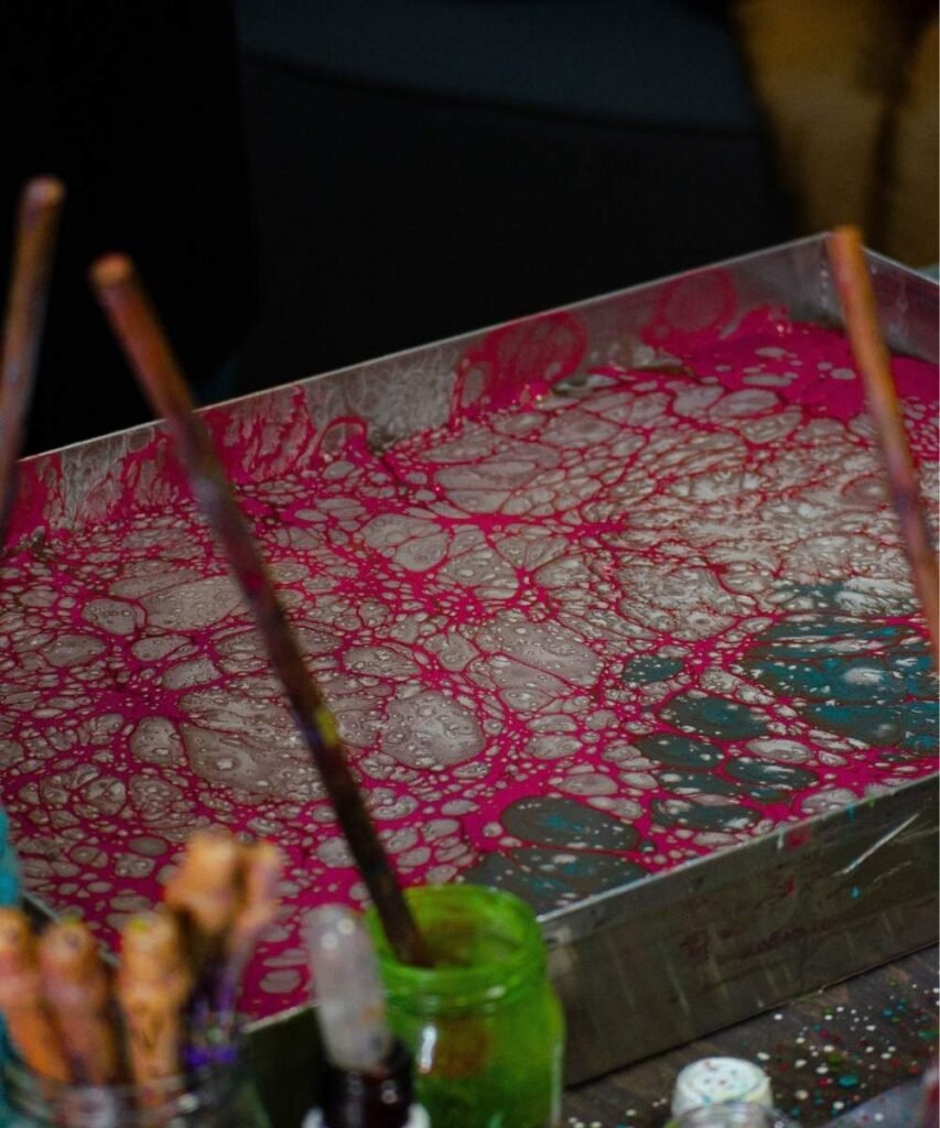 Toddler painting with a wet paintbrush on a dark baking tray during indoor water play