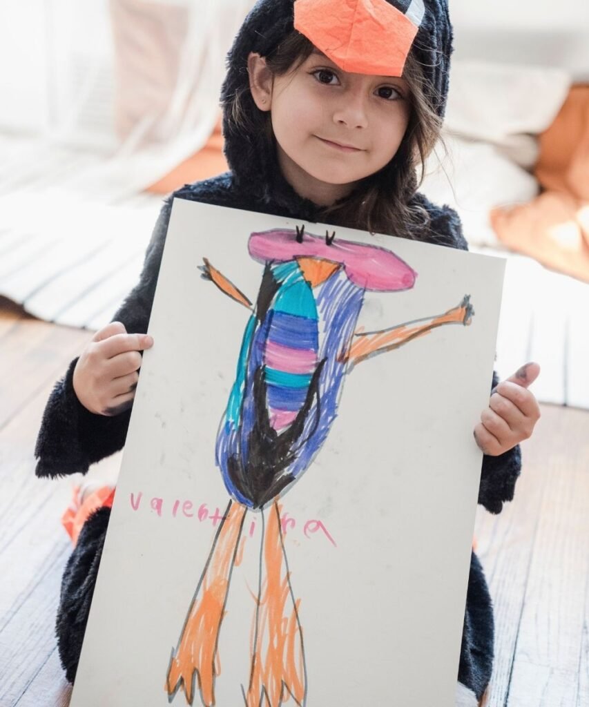Young girl holding up a drawing paper with a colorful scribble turned into a silly creature drawing