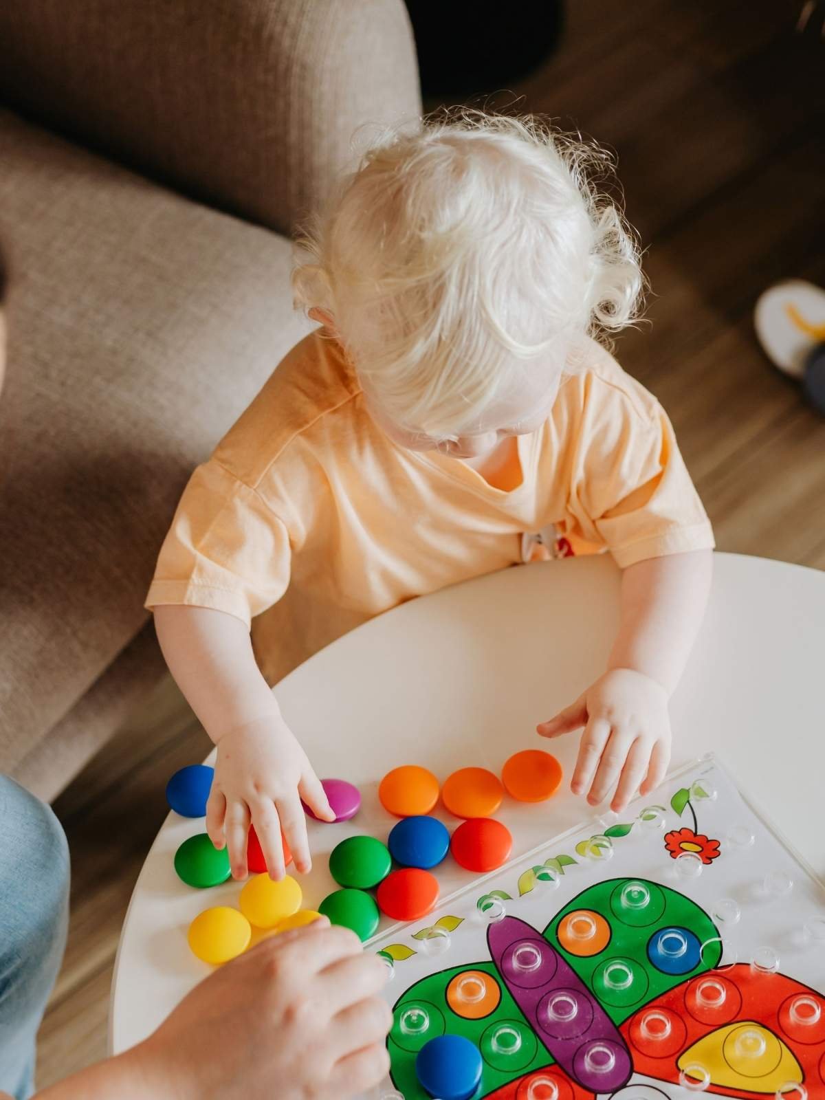 Toddler playing with colorful sensory bin fillers on a table