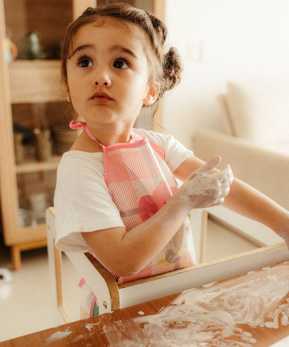 Toddler girl sitting on high chair playing with low mess sensory bin setup