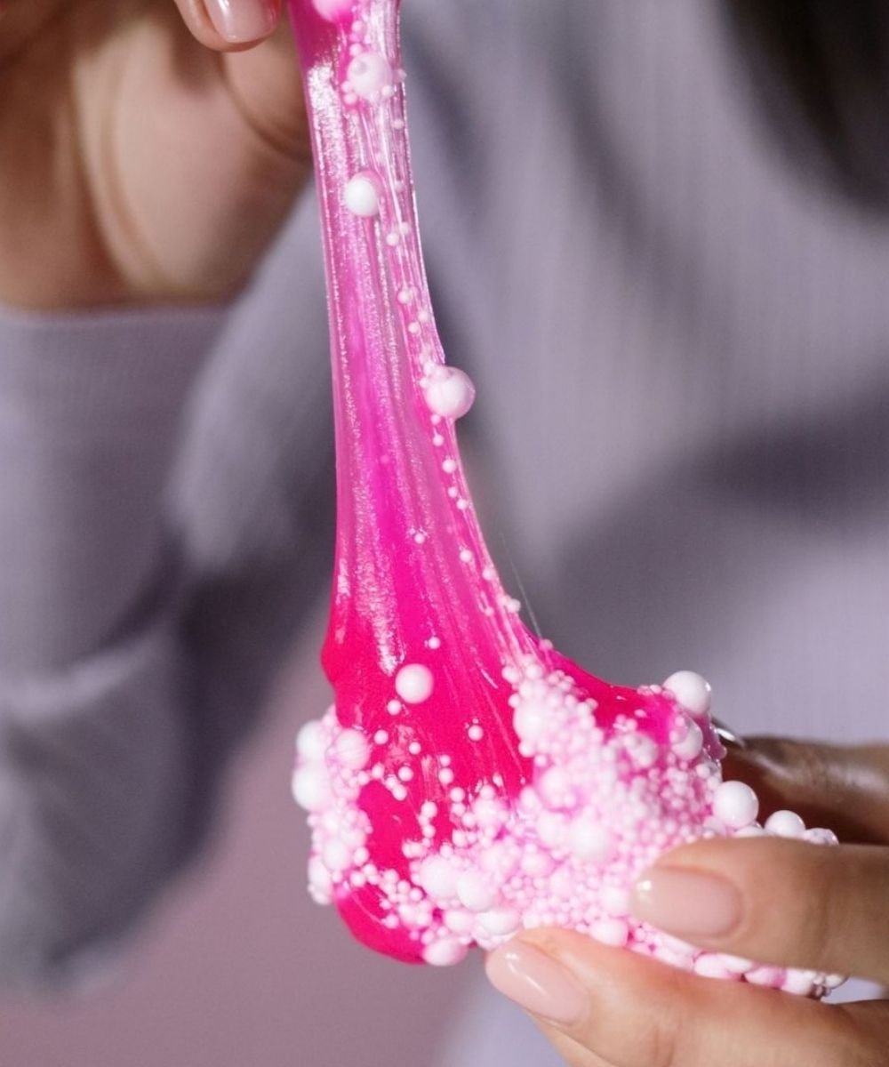 Child stretching pink slime between hands.